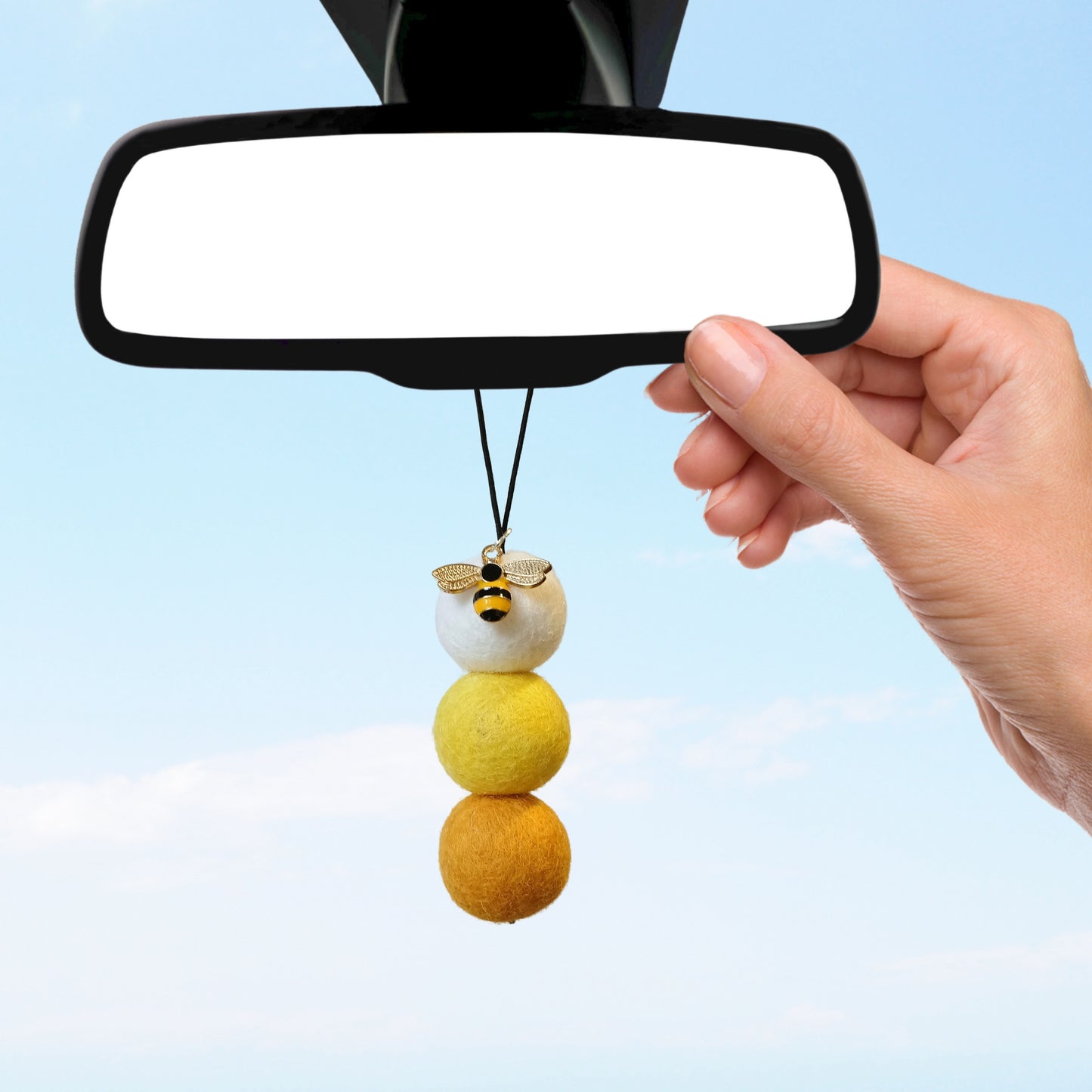 Hand hanging bee charm car diffuser with yellow felt balls on rearview mirror.