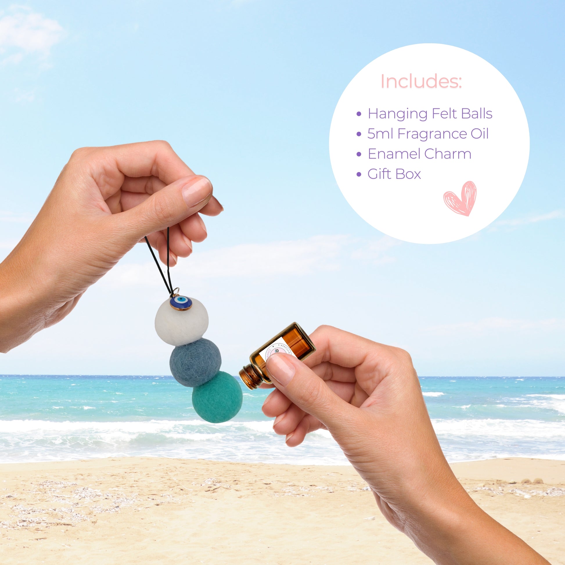Hands apply French Pear fragrance oil to blue felt ball car diffuser with evil eye charm on beach.