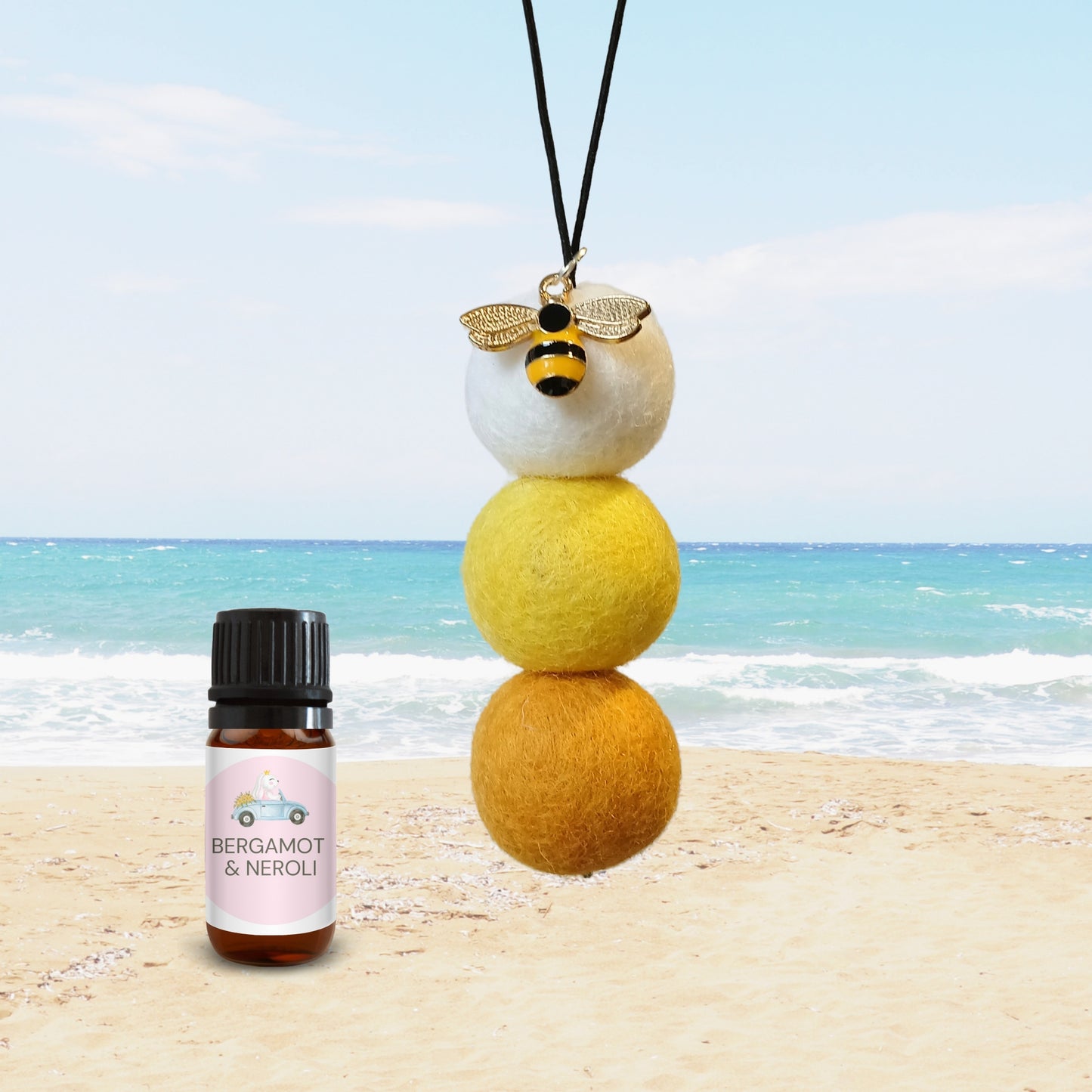 Bergamot and Neroli car diffuser with yellow felt balls and bee charm on sandy beach.