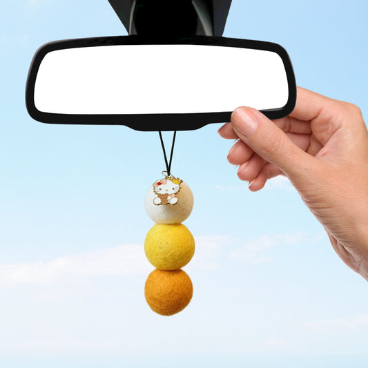 Hand hangs felt ball car air freshener with cinnamon vanilla scent from rearview mirror