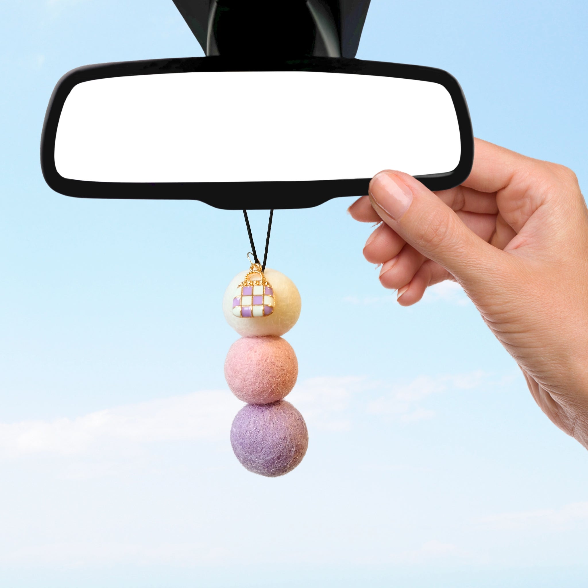 Woman’s hand hanging pastel car diffuser with handbag charm on rearview mirror.